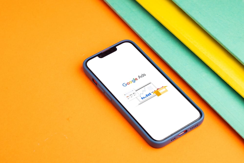 Smartphone showing Google Ads dashboard on a white screen, placed on an orange surface.
