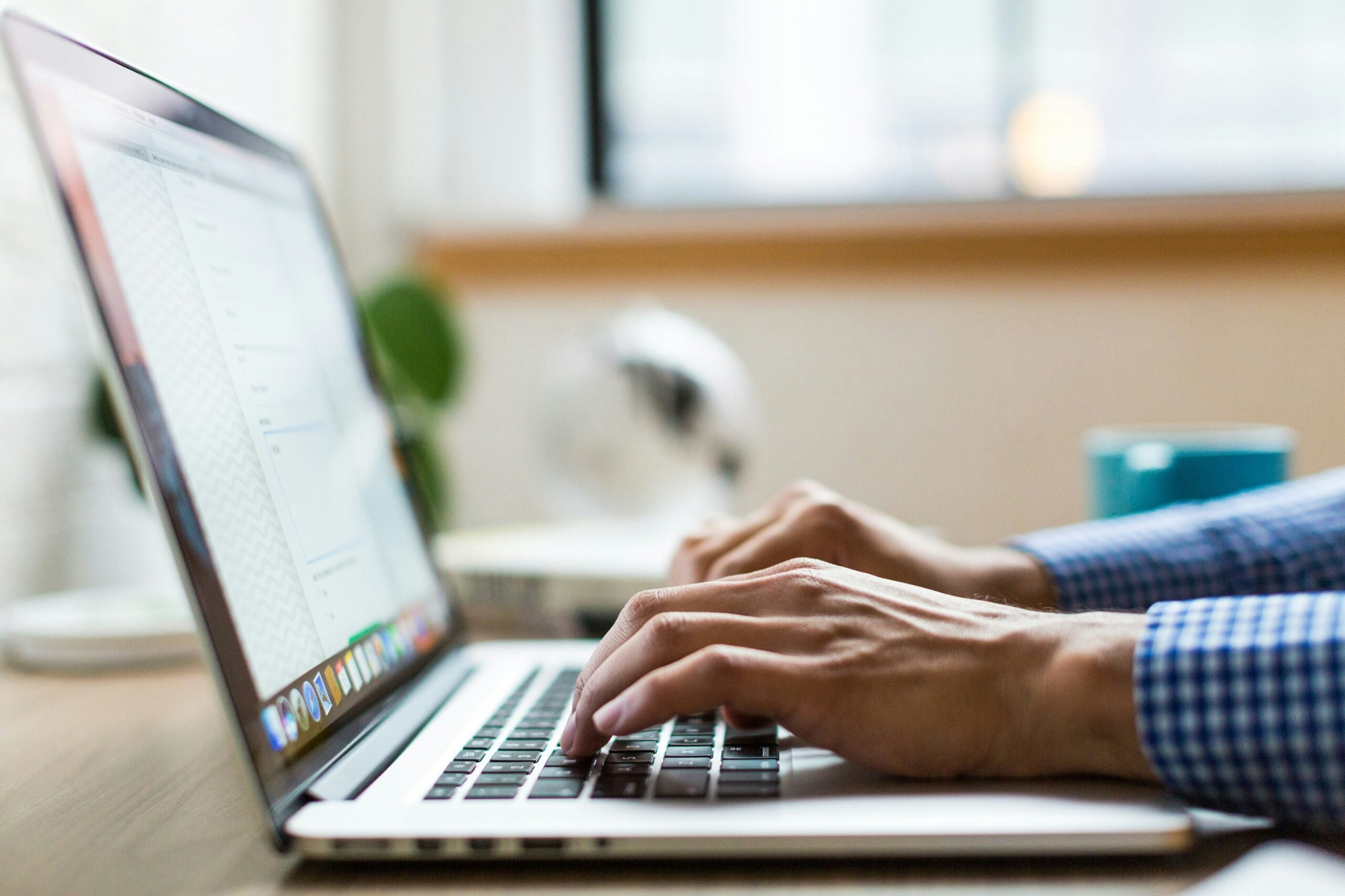 Close-up of hands typing on a laptop keyboard at a desk with a blurred background.
