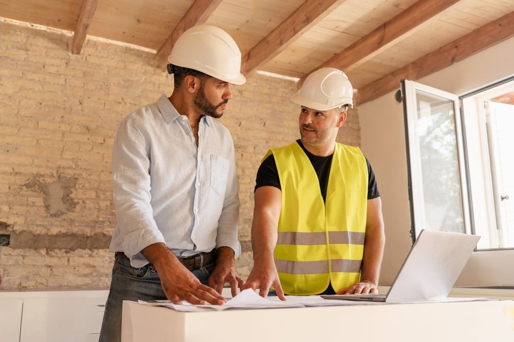 Male Contractor and engineer discussing blueprint using laptop during building construction