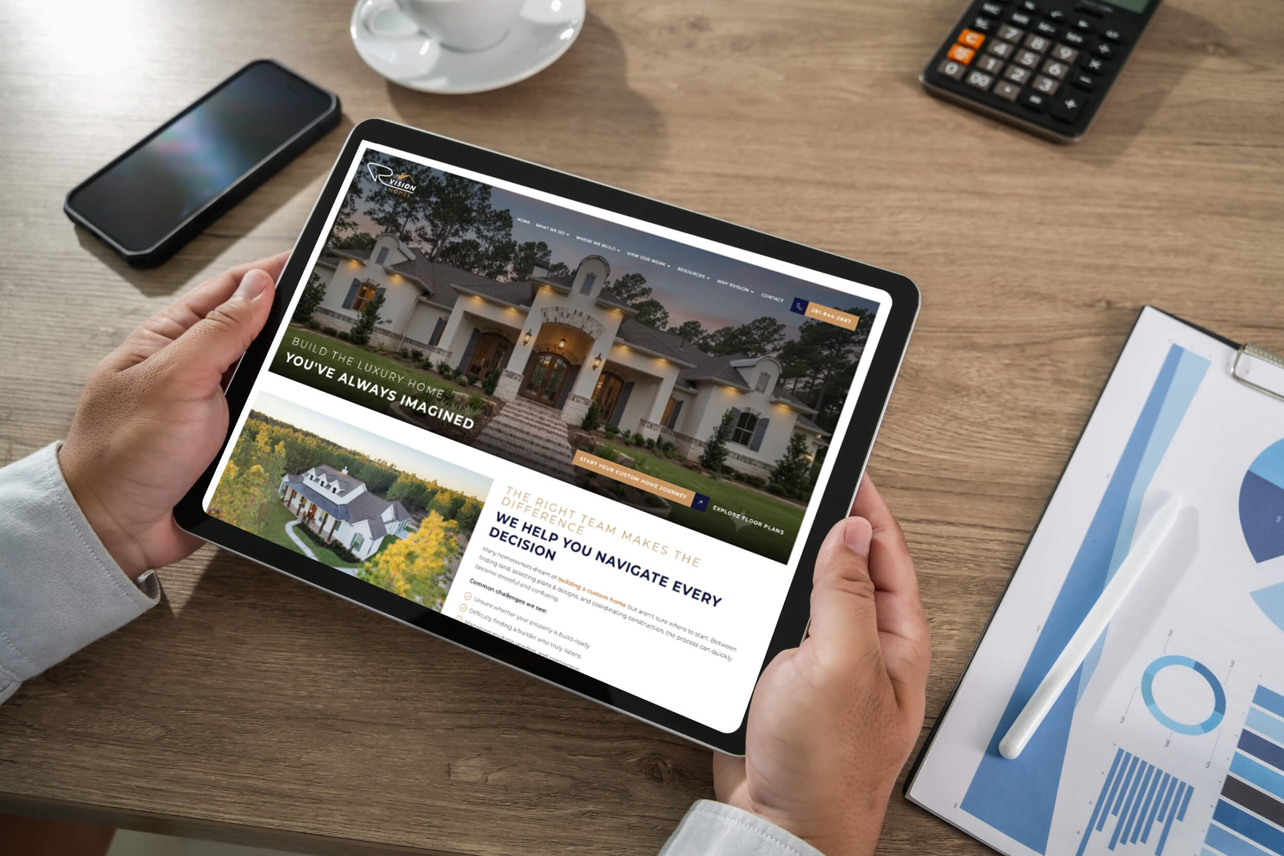 Rvison tablet | itvibes full service digital marketing agency in houston Person Holds a Tablet Showing a Luxury Home Website with a Large Mansion Image and a Navigation Bar at the Top on a Wooden Desk