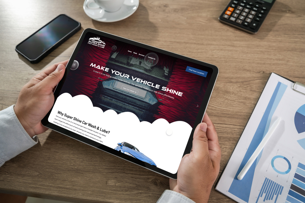 Person is Holding a Tablet That Shows a Car Wash Website with a Bold make Your Vehicle Shine Headline and a White Cloud like Graphic at the Bottom of the Screen