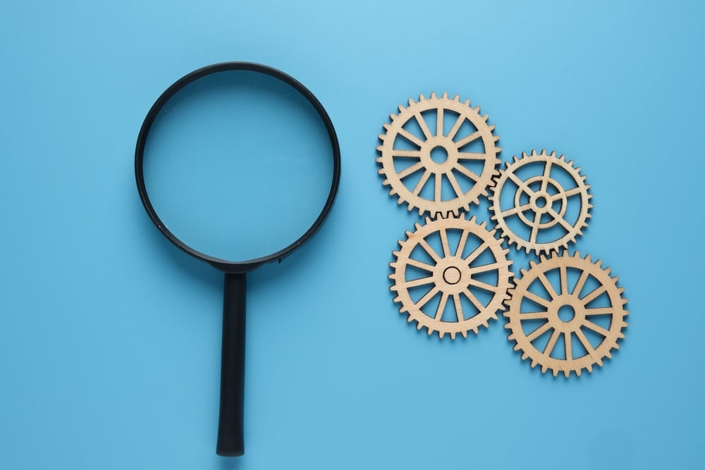 A picture of magnifying glass with arrange gear on blue background. Technical and performance analysis concept.