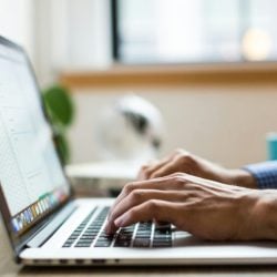 Close-up of hands typing on a laptop keyboard at a desk with a blurred background.