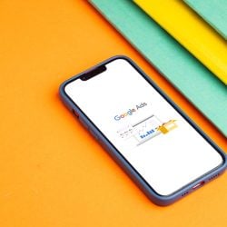 Smartphone Showing Google Ads Dashboard on a White Screen Placed on an Orange Surface