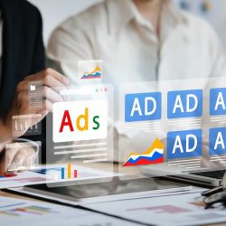 Two professionals reviewing digital ads on a laptop with floating ad icons and graphs from a meeting.